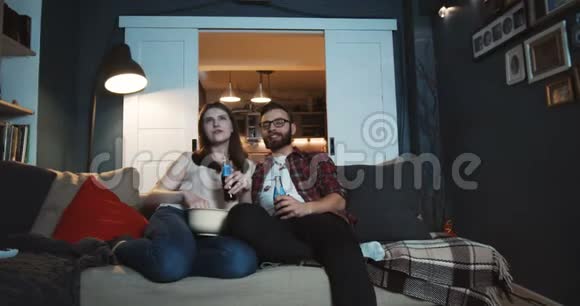 快乐的年轻白种人浪漫的学生夫妇一起在家看电影用投影仪慢动作喝饮料视频的预览图