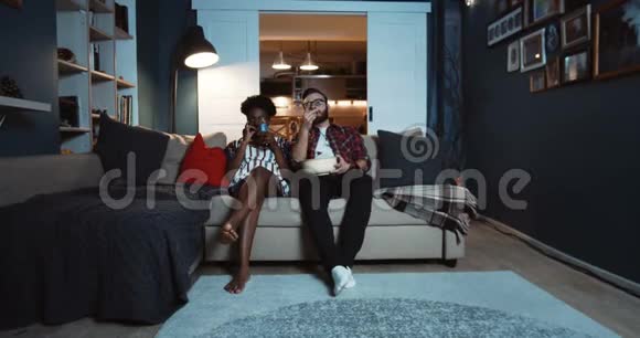 快乐的年轻休闲非洲女人和高加索男人坐在一起看电影爆米花慢动作视频的预览图