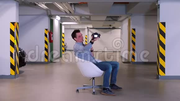 一个男人坐在地下车库里的扶手椅里手里拿着相机视频的预览图