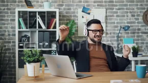 戴着耳机听音乐的快乐男人在工作中开心地微笑视频的预览图