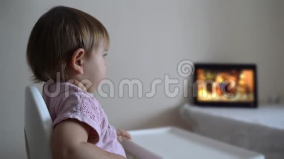 婴儿学步的女孩坐在高椅上在平板电脑上看动画片新一代视频的预览图