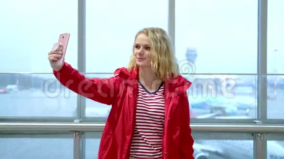 年轻女性博客写手穿着红色冬季服装在机场与追随者交谈现场直播寻找智能手机视频的预览图