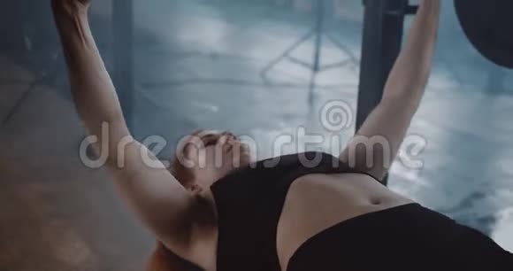 年轻漂亮的白种人红头发的女人举着沉重的杠铃躺在大型专业健身房的长凳上慢动作视频的预览图
