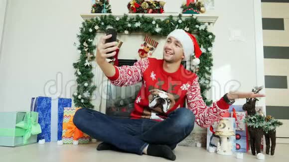 一个穿着新年毛衣和帽子快乐男人用视频链接祝贺他的朋友们过圣诞节用电话视频的预览图