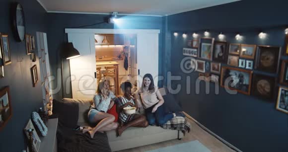 美丽快乐多民族女性朋友笑着在家看大屏幕的喜剧电视剧放映机慢镜头视频的预览图