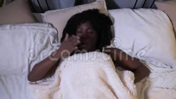 睡眼的年轻黑人妇女躺在大床上打哈欠视频的预览图