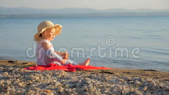 可爱的小女孩坐在海滨小游客坐在红毛巾上看海景夏季或视频的预览图