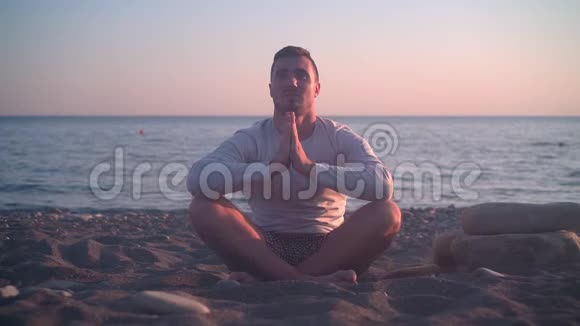 一个年轻人坐在岸边的莲花位置上背景是海上日落人在海滩上沉思视频的预览图
