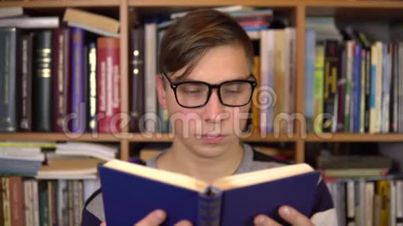一个年轻人读一本书突然在图书馆里砰地一声把它砸了一个戴眼镜的人仔细地看着书看着视频的预览图