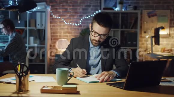 疲倦的商人打哈欠在办公室工作坐在办公桌前写笔记本视频的预览图