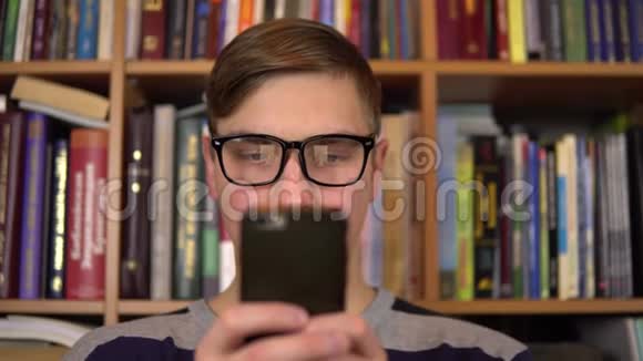 一个年轻人正在图书馆里看智能手机戴眼镜的人仔细地看着手机特写在里面视频的预览图