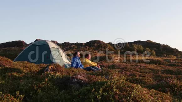 两个年轻的女人坐在旅游帐篷旁边看峡湾视频的预览图