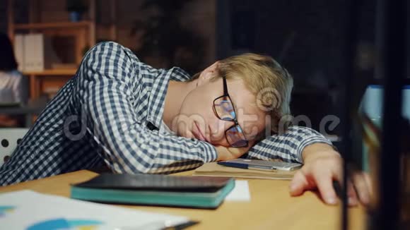 帅哥在黑暗的办公室里睡在桌子上在工作中放松视频的预览图