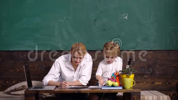 上学教室里有家长的小学生母亲帮助儿子写功课快乐老师帮助小学生视频的预览图