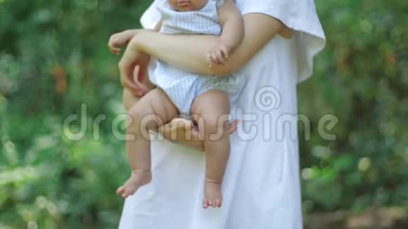 一位年轻的母亲抱着拥抱着她刚出生的女儿双腿抱在公园里绿叶丛中视频的预览图