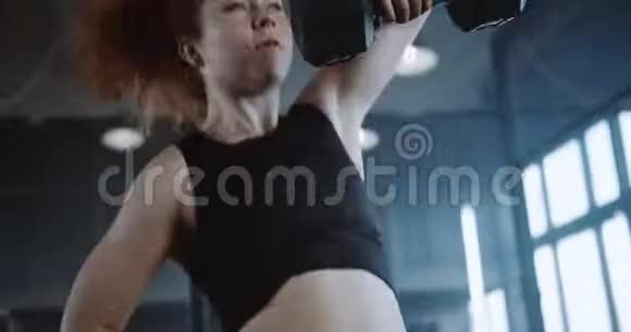 特写年轻的运动白种人红头发运动女子举哑铃在大型专业健身房慢动作视频的预览图