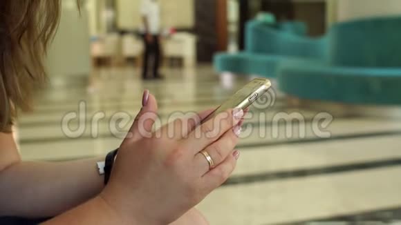 坐在酒店或咖啡厅大厅里的女孩拿着电话的特写镜头视频的预览图