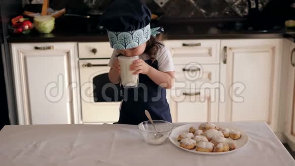 一个小女孩喝牛奶或凯菲尔在厨房里吃饼干视频的预览图