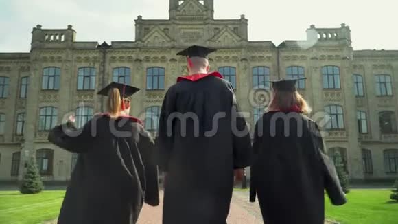 两个快乐的女孩和一个在壁炉里的男孩向大学大楼走去年轻人庆祝他们视频的预览图