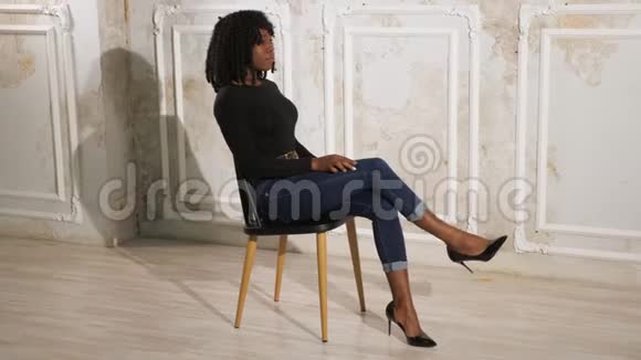 令人兴奋的穿着蓝色牛仔裤的黑人女士坐在棕色木椅上视频的预览图