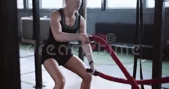 年轻的美丽坚定的运动金发女人用战斗绳锻炼功能训练在大型健身房锻炼视频的预览图
