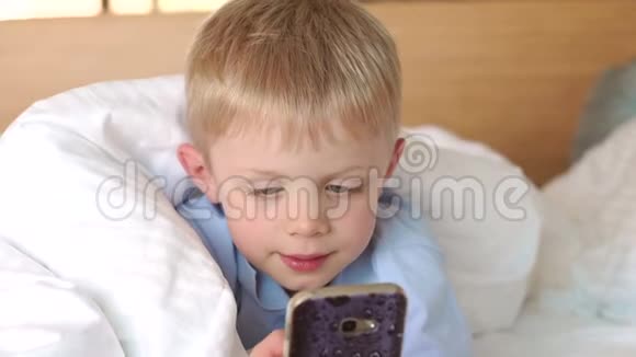 可爱开朗的小孩在电话里玩电子游戏躺在大白床上视频的预览图