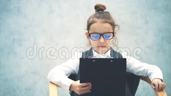 一个女学生商务女孩仔细阅读一个黑色文件夹坐着的女孩是灰色背景戴眼镜严重视频的预览图