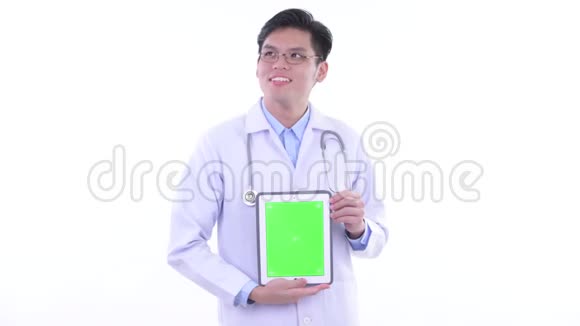 快乐的亚洲青年医生一边讲一边显示数字平板电脑视频的预览图