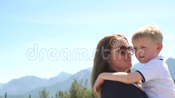 母亲抱着一个孩子在夏天的高山和天空的背景下抱着视频的预览图