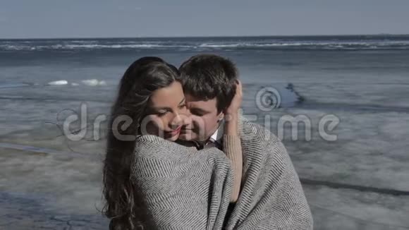 年轻夫妇拥抱着背景是一条覆盖着冰的河流阳光明媚的春天视频的预览图