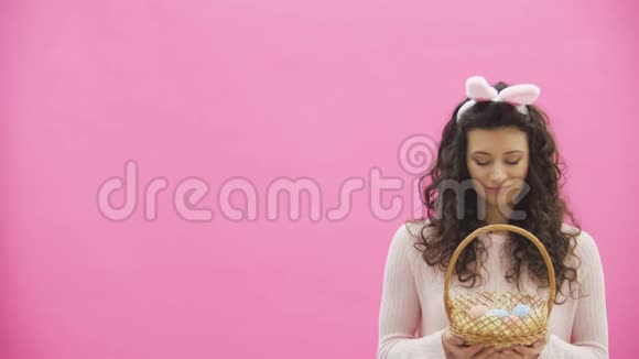 复活节女人的概念可爱的女孩有着兔子的耳朵看着她的鸡蛋盒在粉红色的复活节彩蛋上分离出来视频的预览图