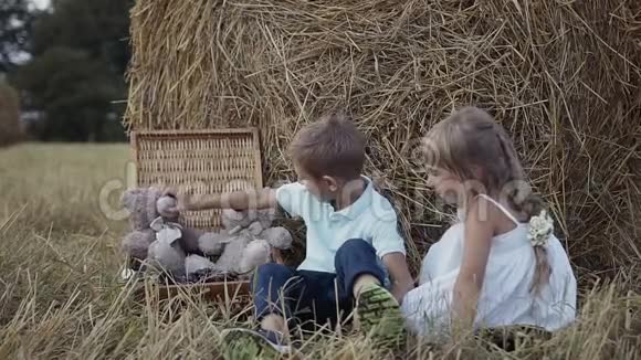 男孩和女孩在玩有趣的软玩具熊穿白色连衣裙的女孩日落视频的预览图