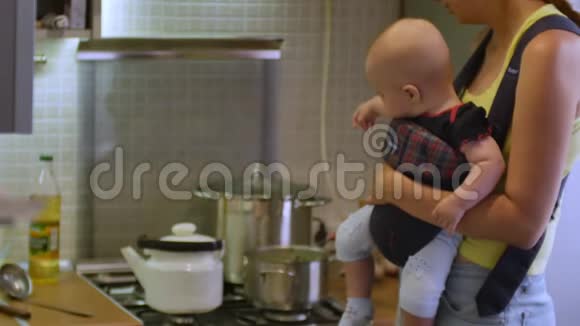 漂亮的女人和一个婴儿坐在婴儿车里煮汤在厨房吃晚饭母亲家庭视频的预览图