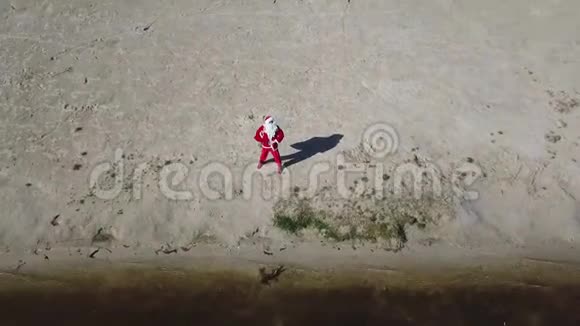 圣诞老人站在湖边的沙滩上手里拿着一个礼品袋圣诞老人拍拍自己的肚子顶部视图视频的预览图