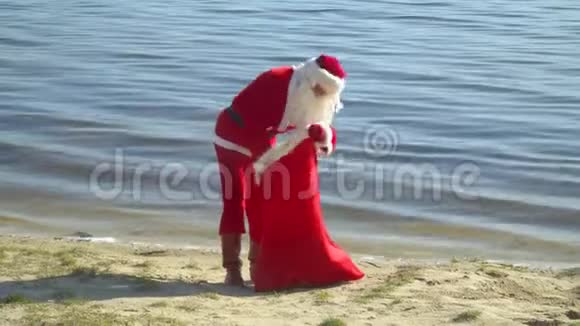 圣诞老人拿着一袋礼物站在海边圣诞老人在一个袋子里找东西并把它绑起来一种腿视频的预览图