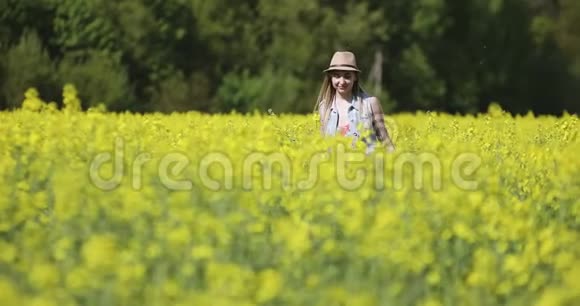 夏天戴着帽子的漂亮女人在油菜花田里走过镜头视频的预览图