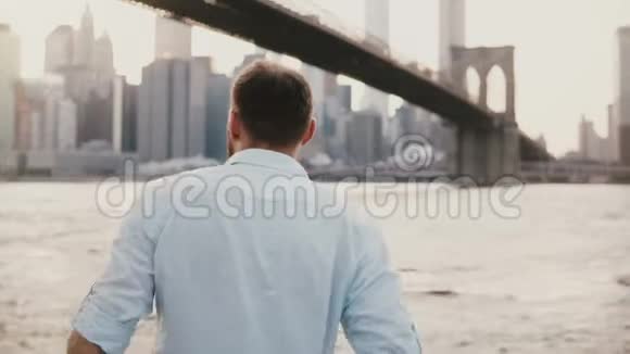 平静的白人年轻人站在靠近纽约市风景的河堤上欣赏4K的景色视频的预览图