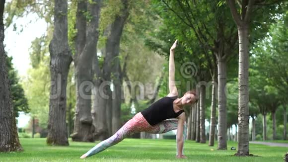 漂亮的运动女孩在公园里慢动作练习瑜伽视频的预览图