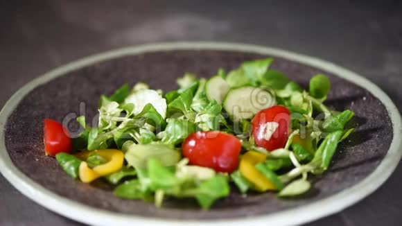 女人在蔬菜沙拉中加入盐与蔬菜黄瓜西红柿胡椒把落在石盘上的绿色沙拉混合在一起视频的预览图