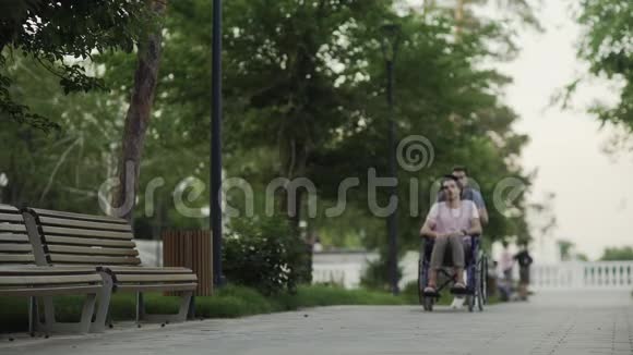 坐轮椅的快乐残疾人和在城市公园跑步的快乐年轻人视频的预览图