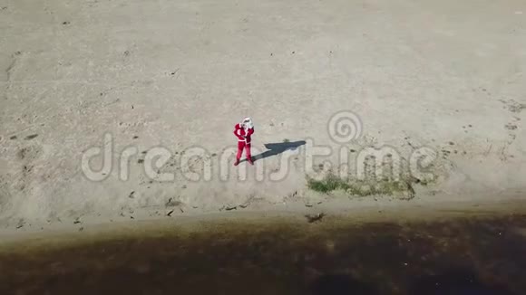 圣诞老人站在湖边的沙滩上手里拿着一个礼品袋圣诞老人在镜头前打招呼和打手势视频的预览图