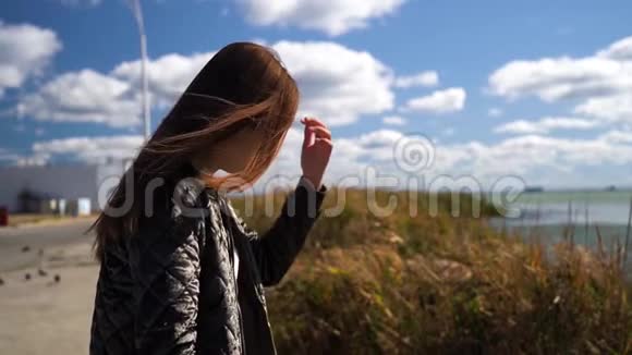 穿绿色夹克的年轻女孩或女人修头发多云的天空和湖泊景色不错慢动作视频的预览图