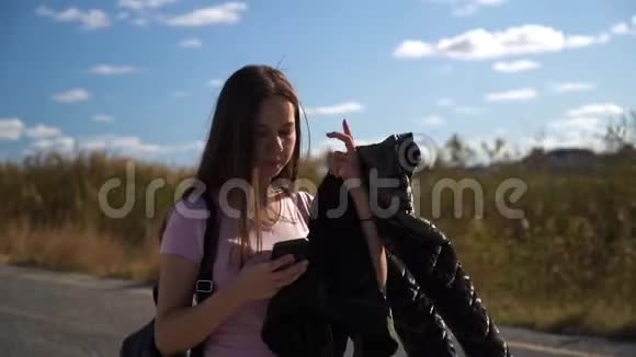 手拿夹克的女孩用手机走路视频的预览图