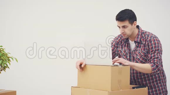 专注的年轻人站着用笔记本电脑在一堆箱子上寻找合适的公寓搬家打电话视频的预览图