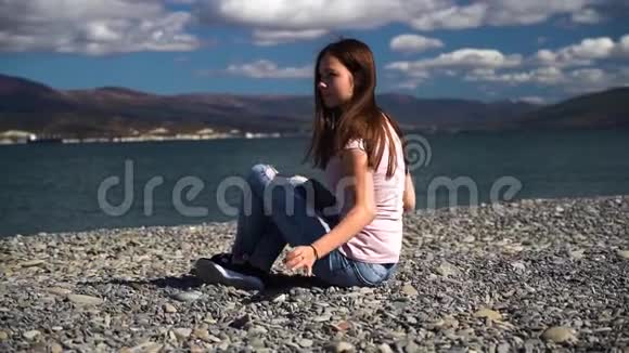 年轻而迷人的女孩靠在海滩上慢镜头地看着镜头秋天的天气视频的预览图