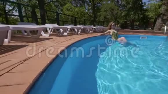 年轻的金发女郎在夏日独自一人在游泳池里放松斜倚在边上视频的预览图