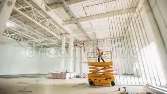 在宽敞的房间里安装剪刀升降机的建筑工人视频的预览图