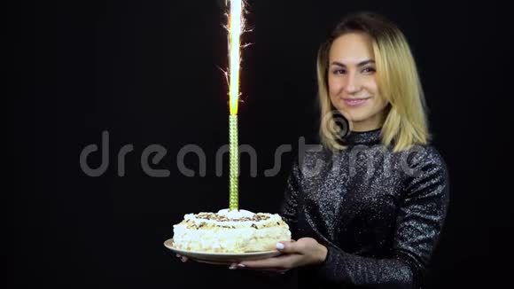 那个女孩拿着一个带烟火的节日蛋糕一个年轻的女人站在一件闪亮的晚礼服上孤立的黑色视频的预览图