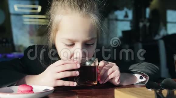 可爱小女学生坐在桌子旁吃马卡龙喝茶女孩吃健康食品视频的预览图