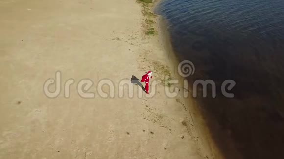 圣诞老人站在湖边的沙滩上手里拿着一个礼品袋圣诞老人纠正他的帽子热带的圣诞老人视频的预览图